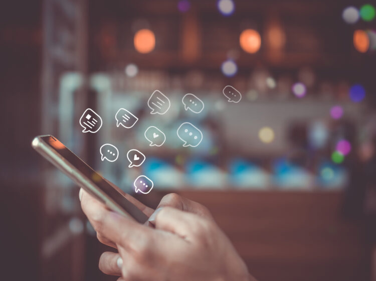 Women hand using smartphone typing, chatting conversation in chat box icons pop up. Social media maketing technology concept.Vintage soft color tone background.